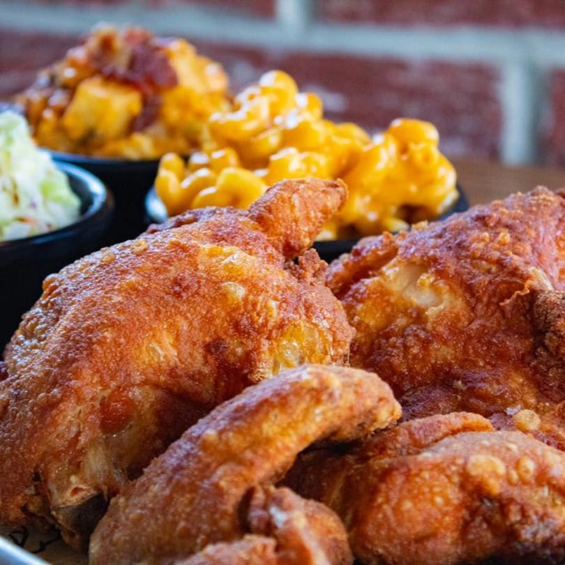 Crispy fried chicken pieces with sides of mac and cheese, baked beans, and coleslaw.