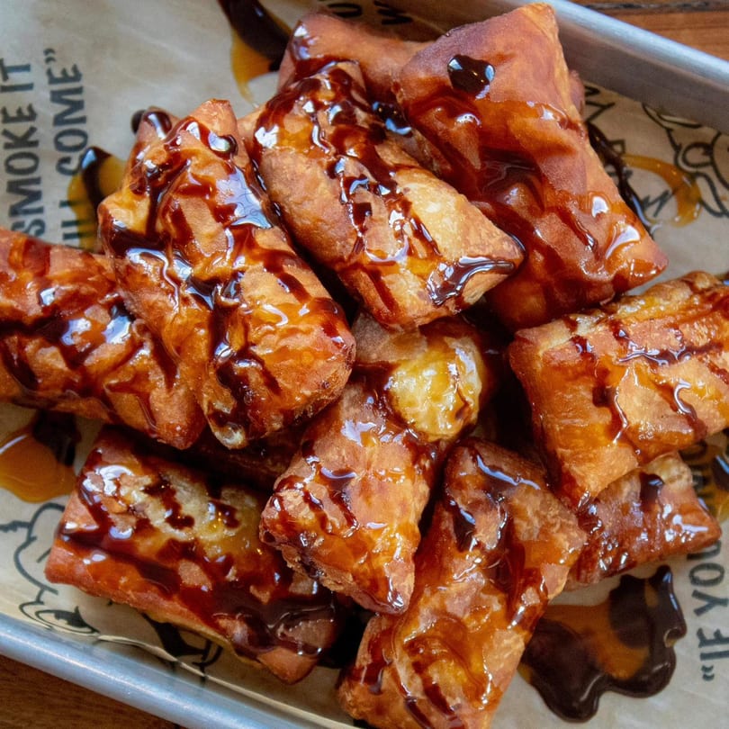 BBQ King Smokehouse's fried dessert bites, drizzled with sweet caramel and chocolate sauce, on a metal tray.