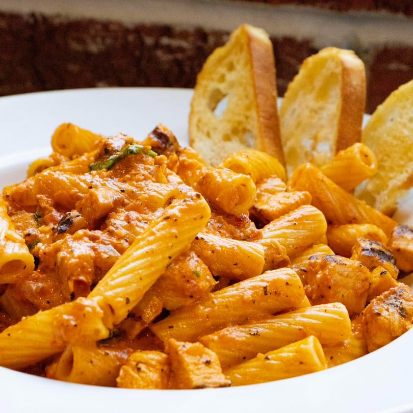 Rigatoni pasta with a creamy orange sauce, chicken pieces, and three slices of toasted bread.